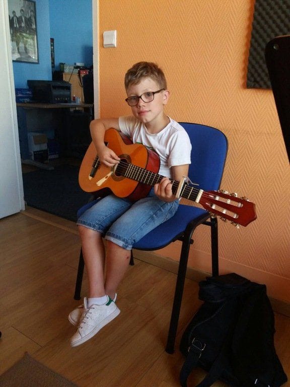 Un jeune élève joue de la guitare classique, assis.