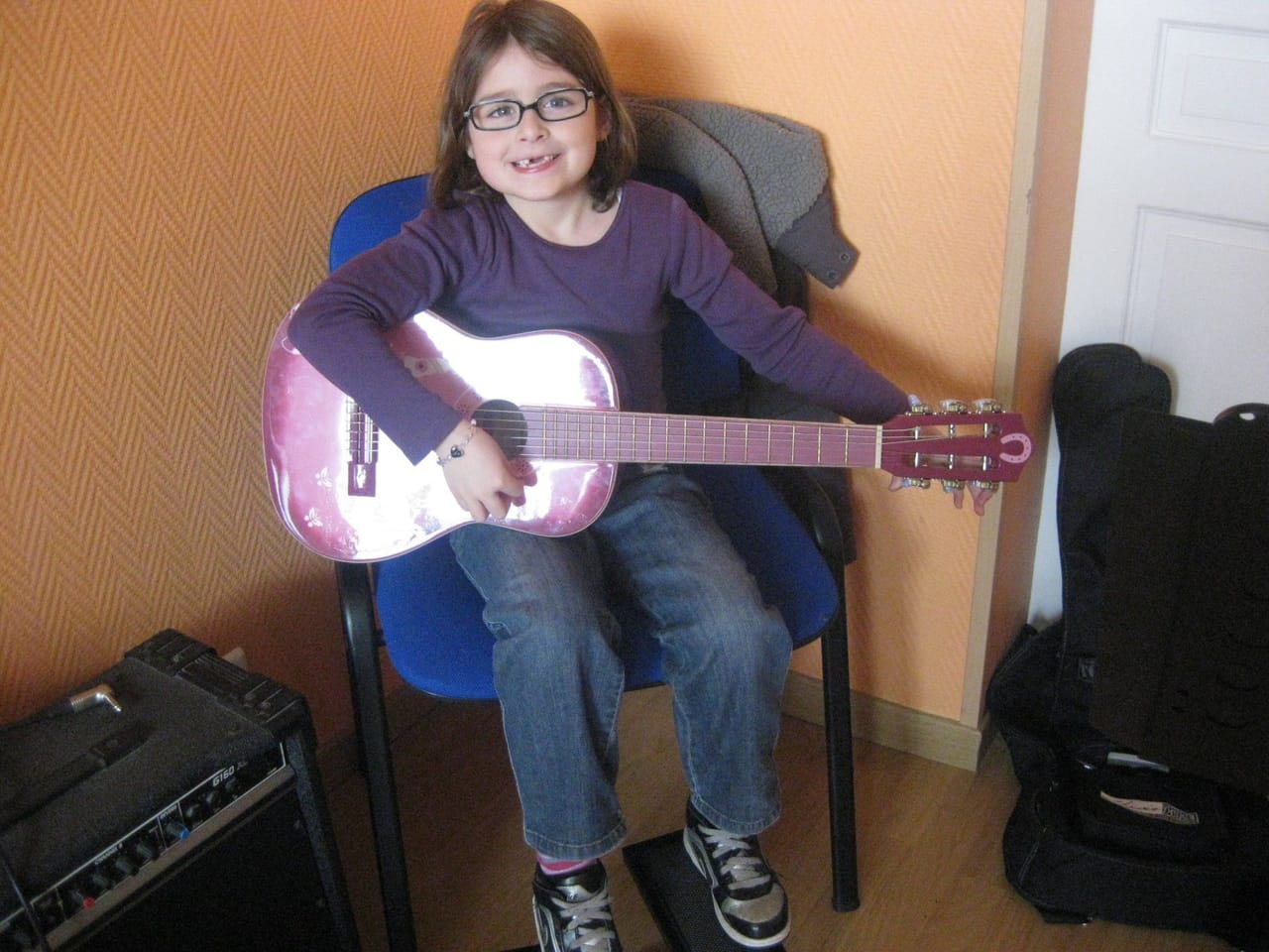 Une jeune élève joue de la guitare acoustique en souriant.