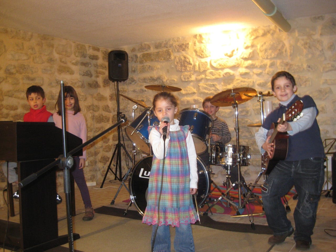 Une petite fille chante au micro sur scène, accompagnée d’un groupe.